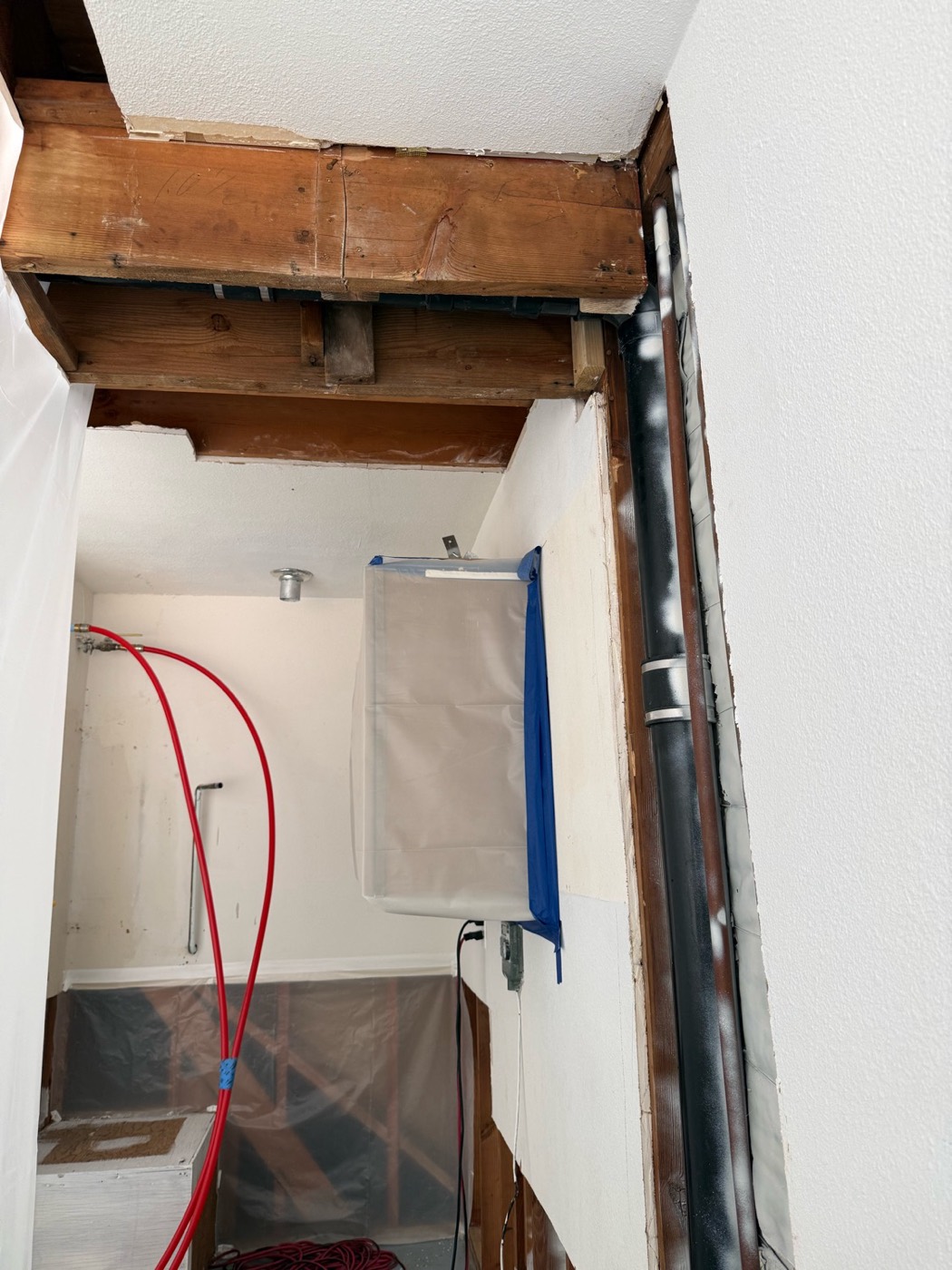 Opened ceiling and wall framing exposed for drying, with containment plastic hung