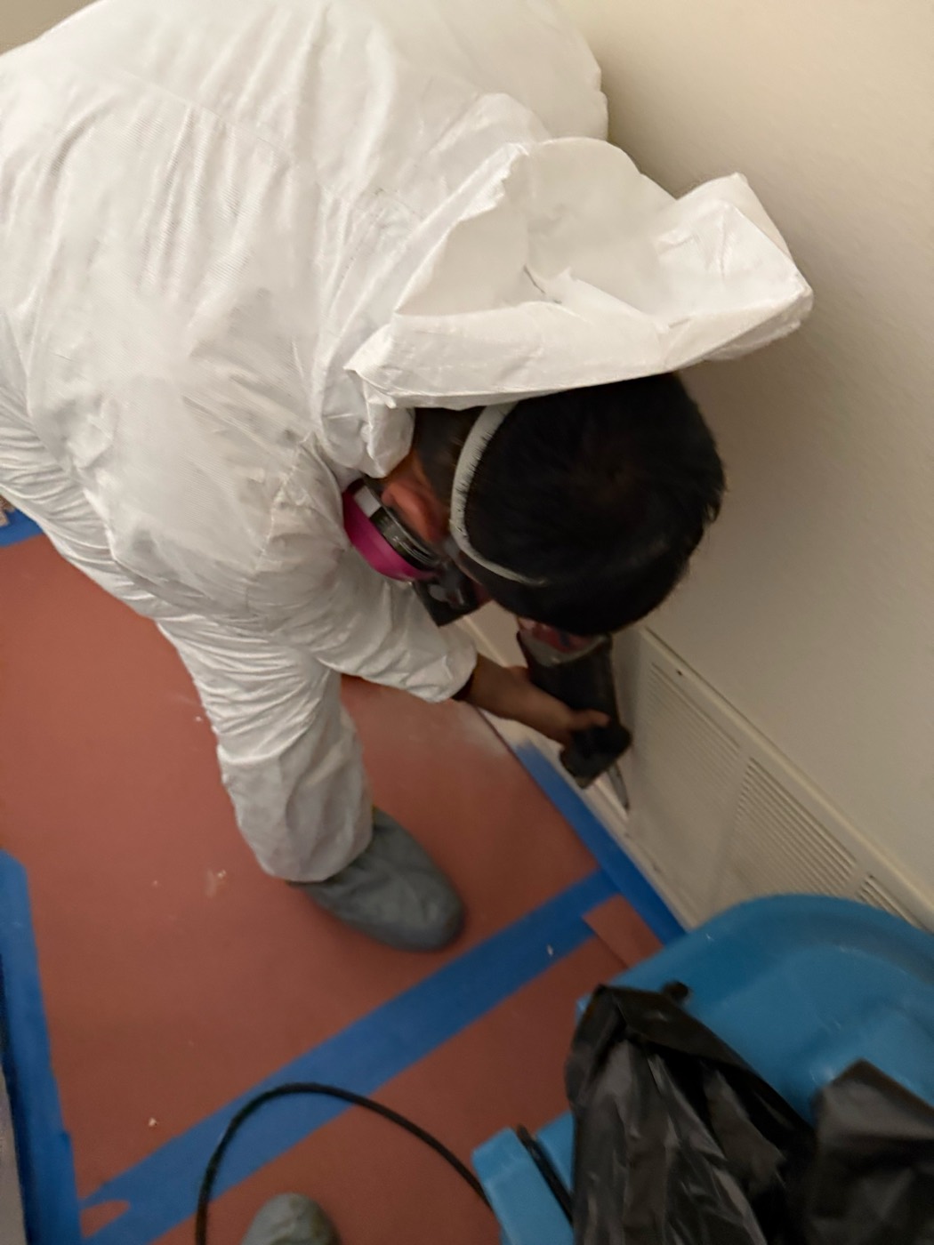 Technician in full protective suit and respirator performing controlled demolition inside taped containment